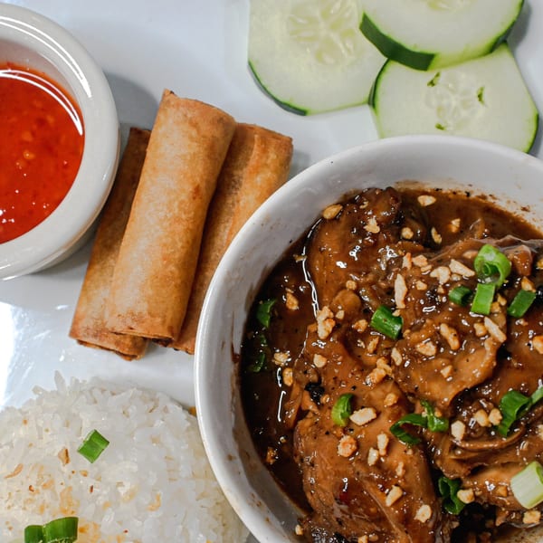 Filipino adobo with rice, lumpia, sweet chili sauce, and cucumber slices on a white plate.