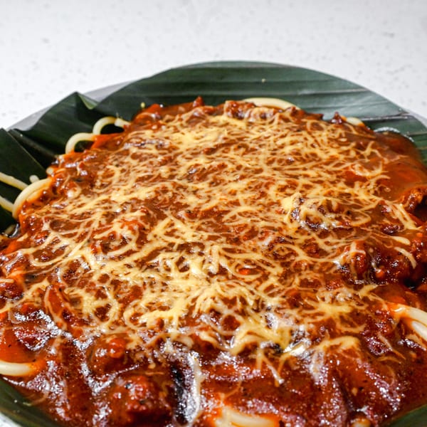 Spaghetti with a rich red sauce and melted cheese, served on a banana leaf.