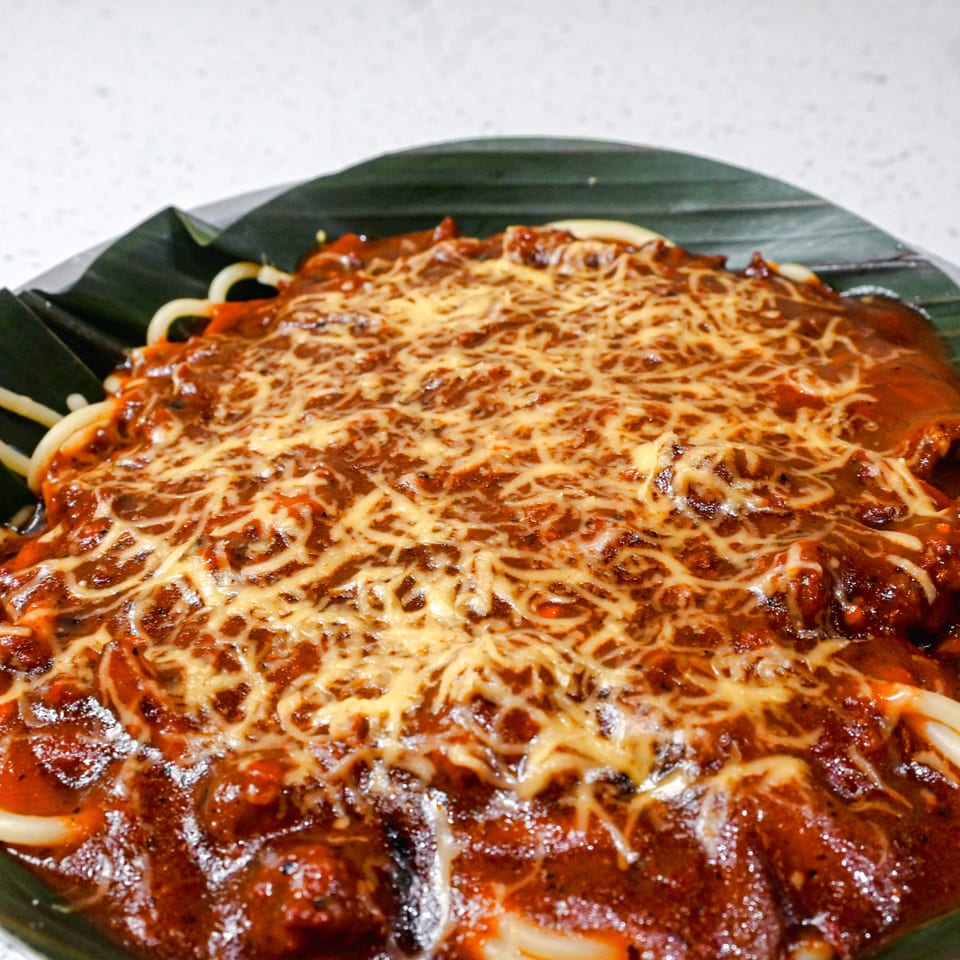 Spaghetti with a rich red sauce and melted cheese, served on a banana leaf.