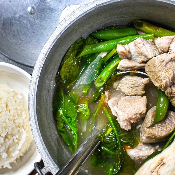 A close-up of a pot of pork and green vegetable stew with a side of rice.