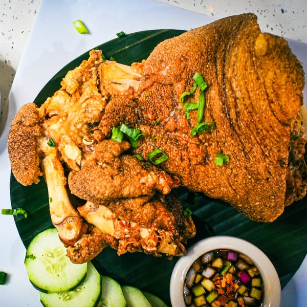 Crispy pata, a deep-fried pork hock, garnished with green onions, cucumber slices, and dipping sauce.