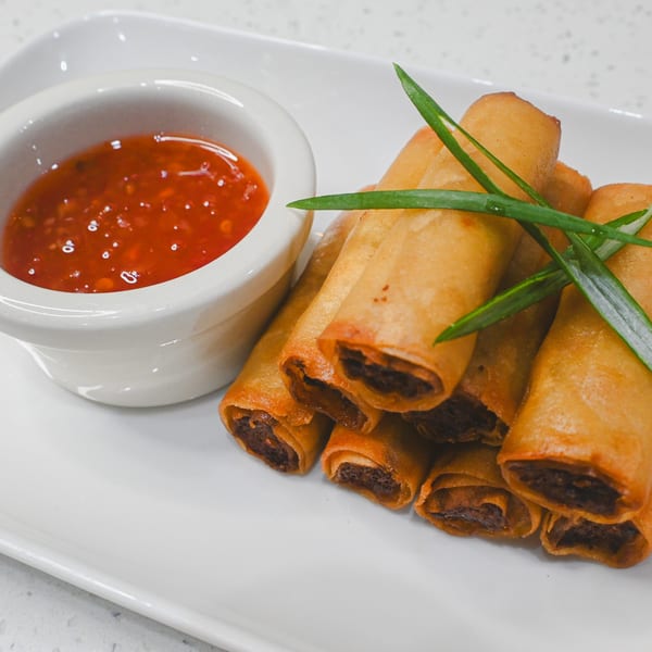 Crispy golden spring rolls with green onion garnish and a side of sweet chili dipping sauce.