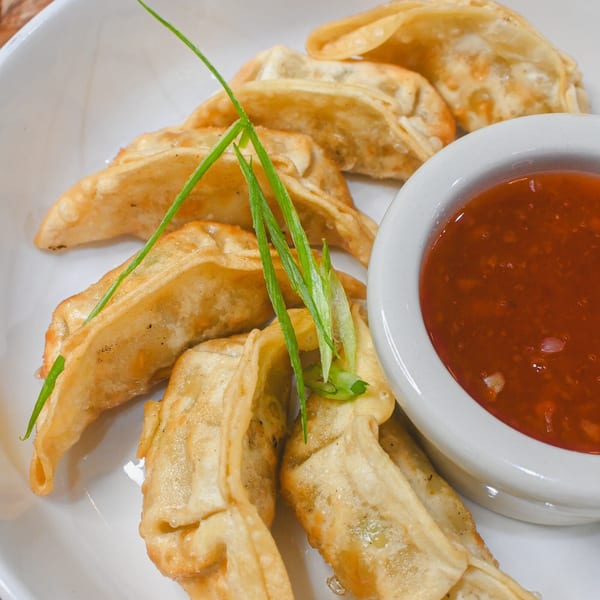Crispy fried dumplings garnished with green onions, served with a side of red dipping sauce.